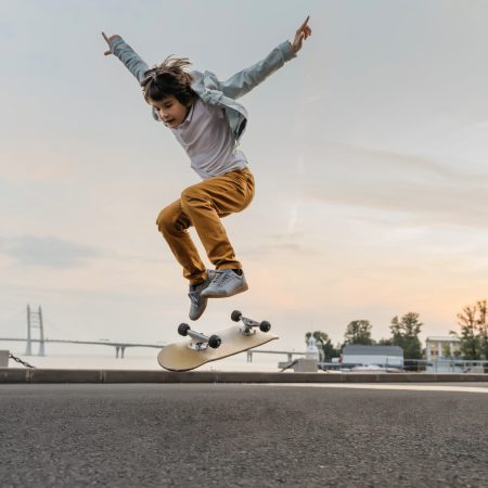 Boy jumping on skateboard at the street. Funny kid skater practicing ollie on skateboard at sunset.