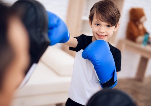 The father is training his son boxing. In the hands of the boy boxing gloves. They go in for sports at home.