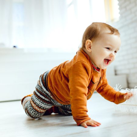 Happy child in orange sweater plays with feather on the floor