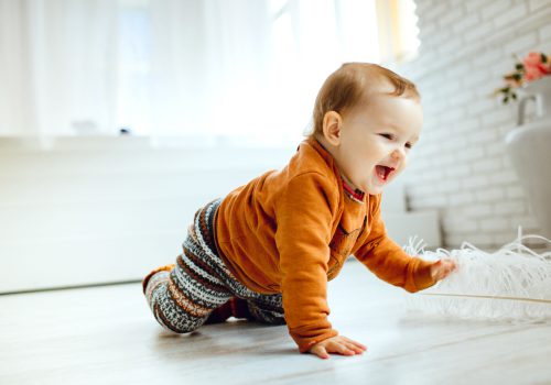 Happy child in orange sweater plays with feather on the floor
