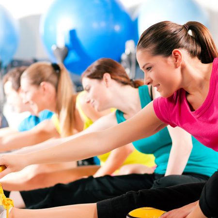 Group of four people in colorful cloths in a gym doing aerobics or warming up with gymnastics and stretching exercises